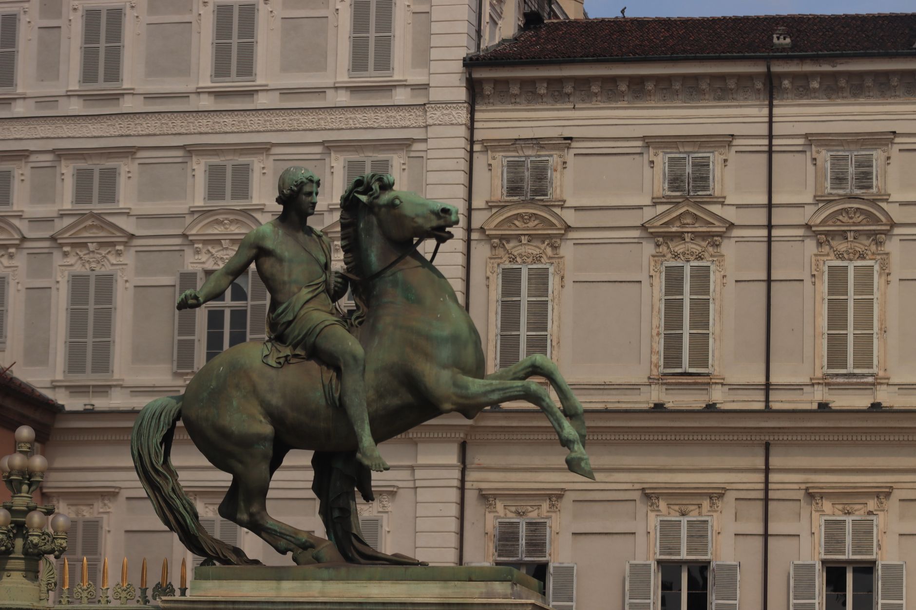 Bronze sculpture of a horseman in front of a historic palace facade.